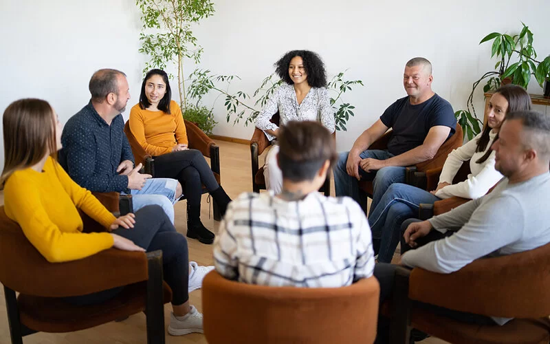Eine Gruppe Co-Abhängiger sitzt auf Stühlen in einem Kreis und spricht miteinander.