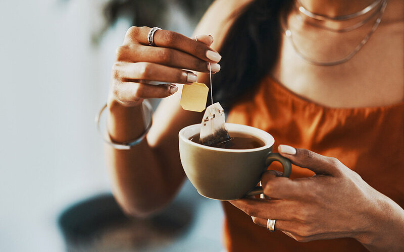 Eine Frau hält eine Tasse Schwarztee mit Teebeutel in der Hand.