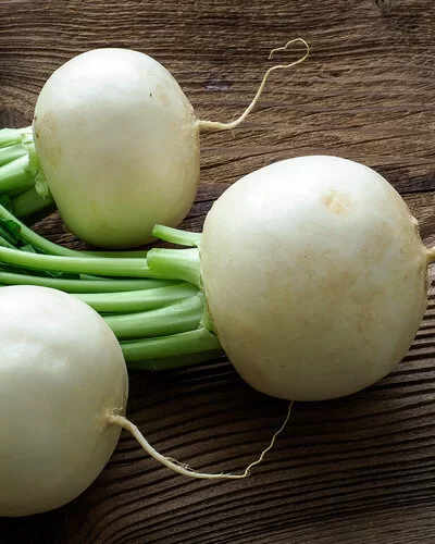 3 frische Mairüben mit Stielen und Blättern liegen auf einem Holzuntergrund.