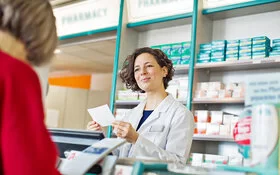 Eine Apothekerin hat ein Rezept einer Kundin in den Händen und lächelt.