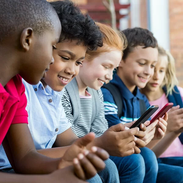 Fünf Jungen und Mädchen aus der dritten oder vierten Klassenstufe sitzen nebeneinander und schauen auf Smartphones.