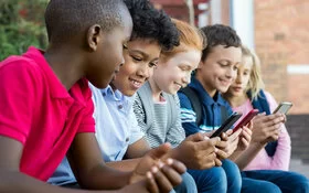 Fünf Jungen und Mädchen aus der dritten oder vierten Klassenstufe sitzen nebeneinander und schauen auf Smartphones.