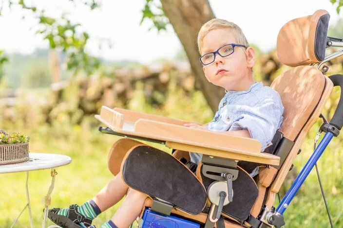 Ein Junge sitzt in der Natur auf einer Sitzhilfe.