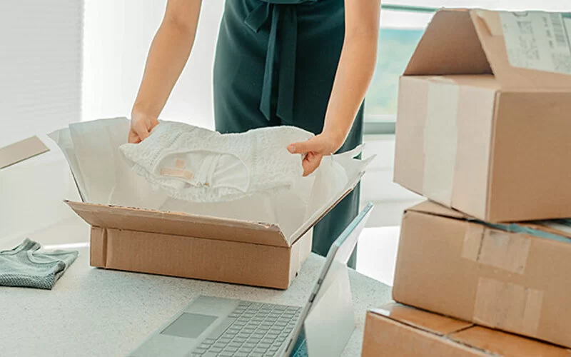 Mehrere Pakete vom Online-Shopping sind im Raum verteilt, eins wird gerade von einer Person ausgepackt