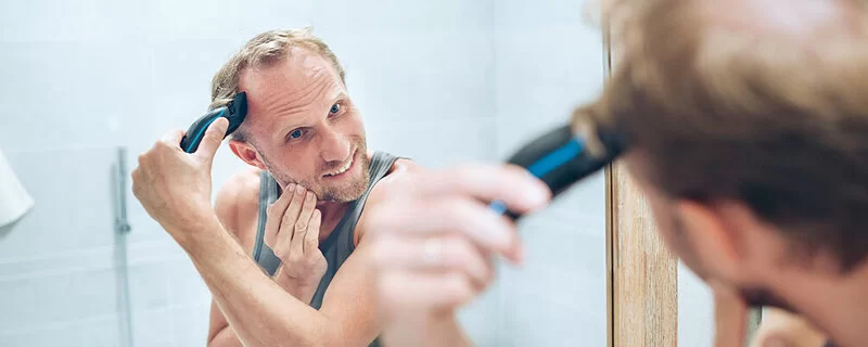 Mann mit Haarausfall rasiert sich die Haare.