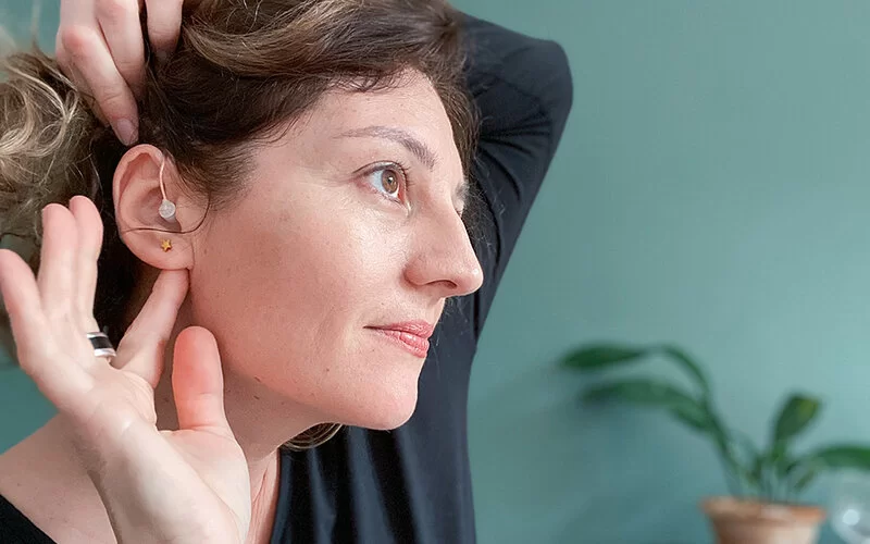 Eine Frau trägt ein Hörgerät und berührt ihr Ohr.