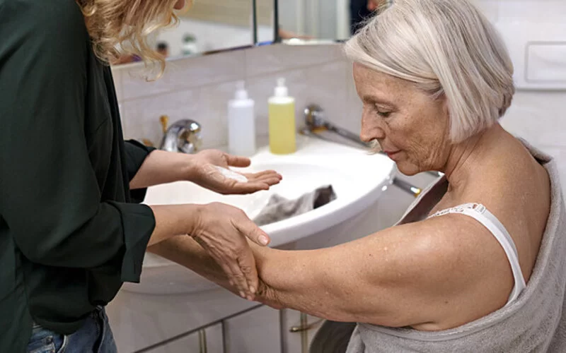 Eine Frau trägt einer älteren Frau, die unter Diabetes leidet, Creme auf die trockene Haut auf.