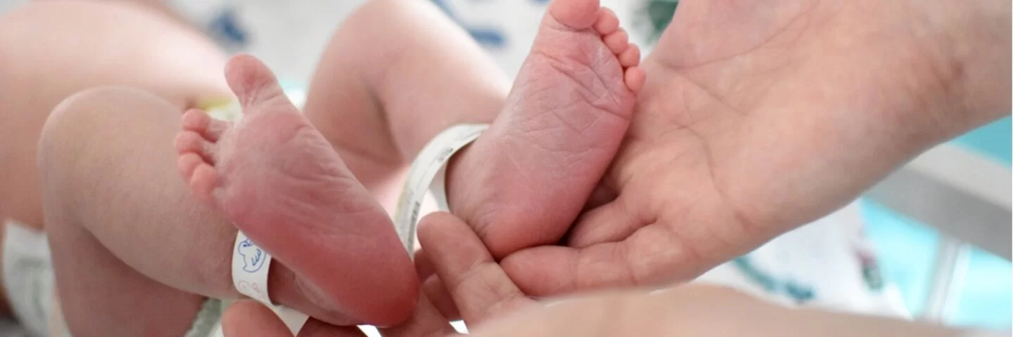 Neugeborenes wird an den Füßen gehalten