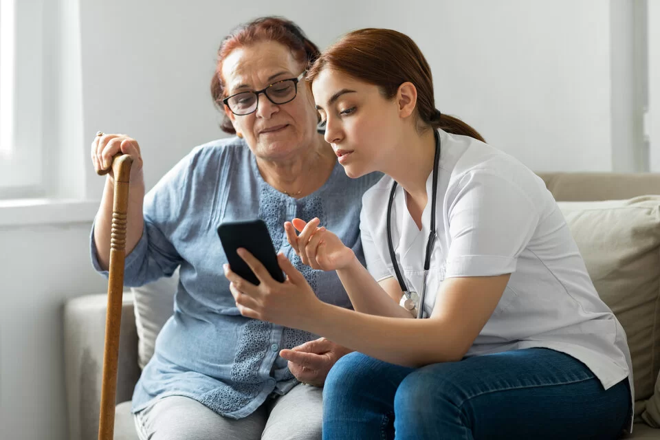 Eine ältere und eine jüngere Frau schauen auf das Display eines Smartphones.