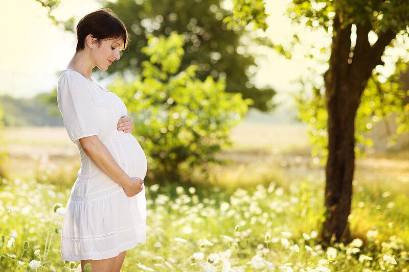Eine schwangere Frau steht in einem weißen Kleid auf einer Wiese