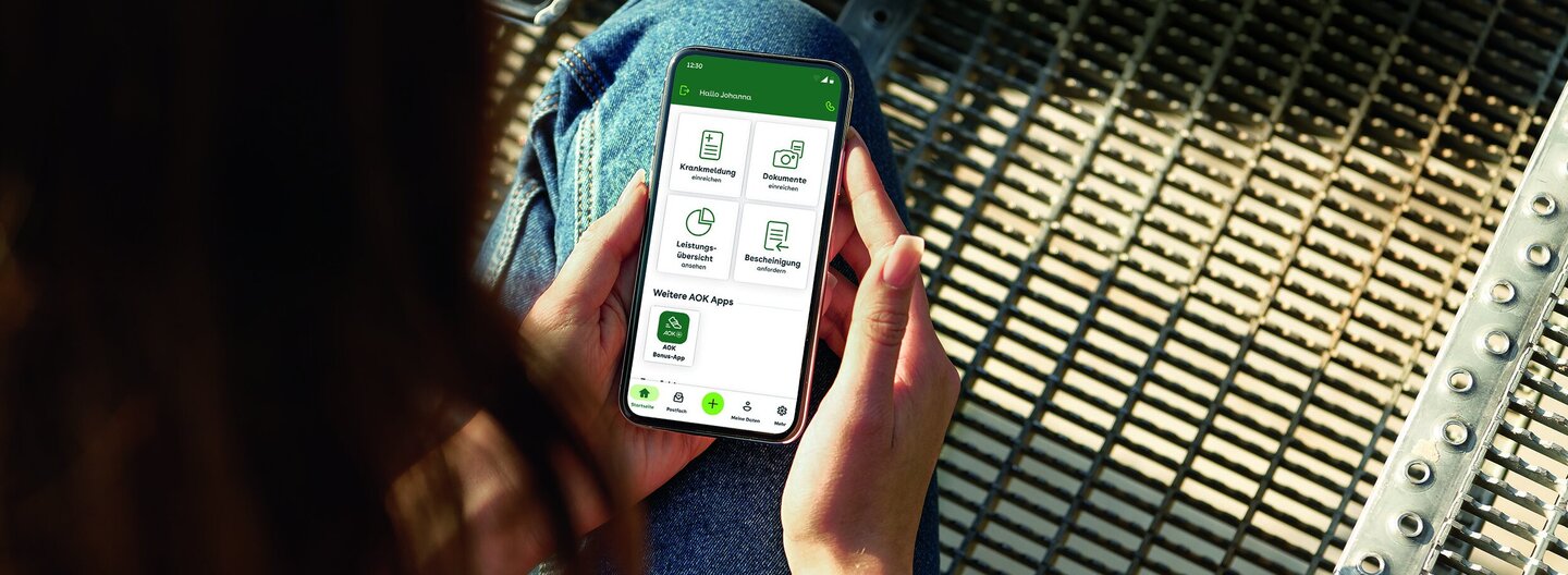 Eine junge Frau blickt auf ihr Smartphone. Mit dem Portal “Meine AOK” hat sie alle Informationen griffbereit.