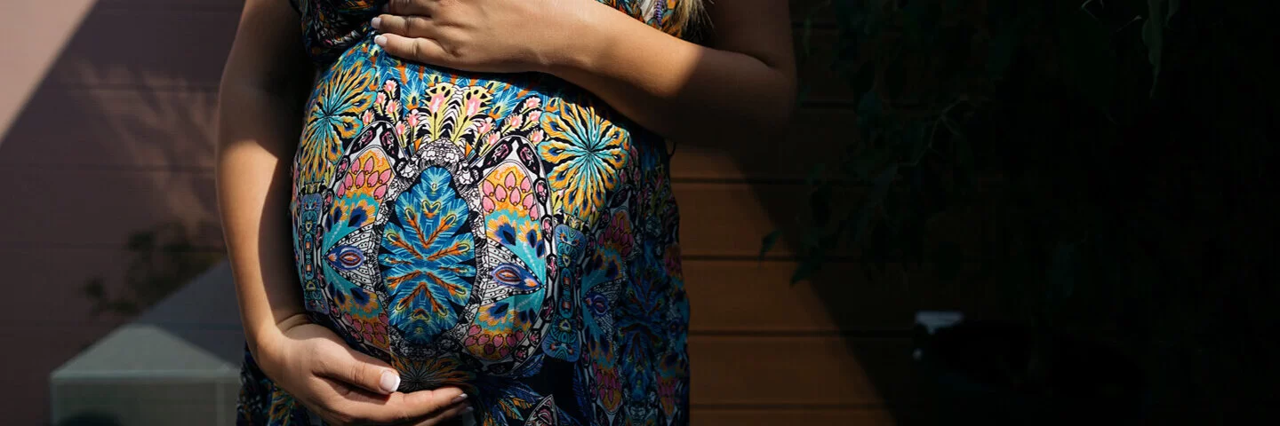 Eine Schwangere in einem Kleid mit Muster umfässt ihren Bauch.