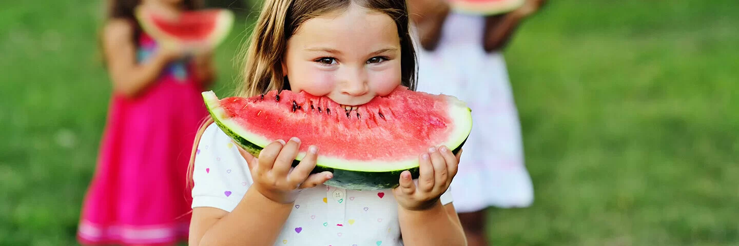 Ein Mädchen isst Wassermelone im Park mit ihren Freundinnen.