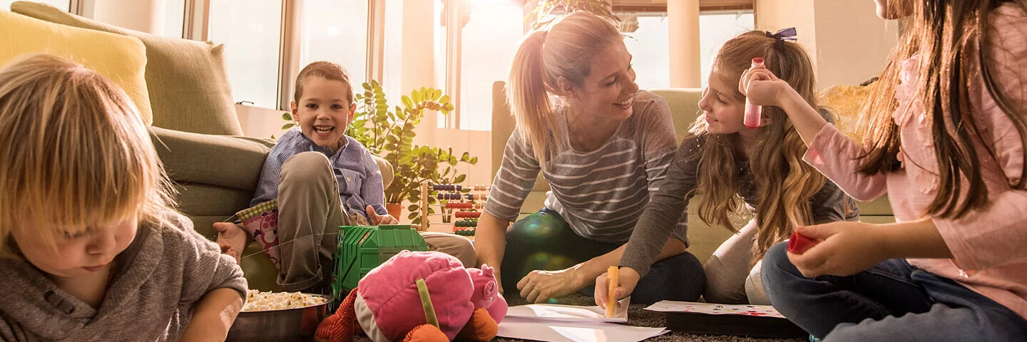 Eine Tagesmutter sitzt mit Kindern ihrer Gruppe zusammen und malt.