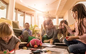 Eine Tagesmutter sitzt mit Kindern ihrer Gruppe zusammen und malt.