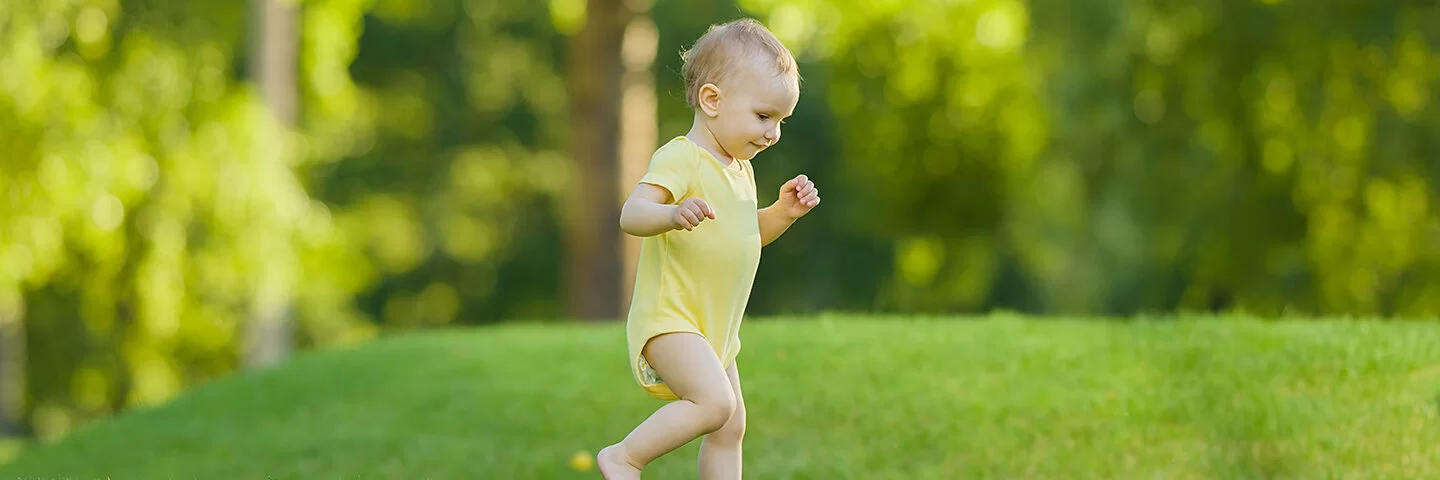 Baby lernt laufen und geht erste Schritte allein im Garten auf einer Wiese.