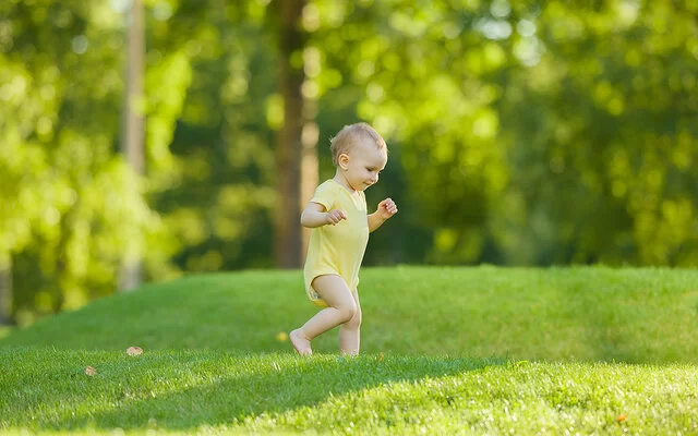 Baby lernt laufen und geht erste Schritte allein im Garten auf einer Wiese.