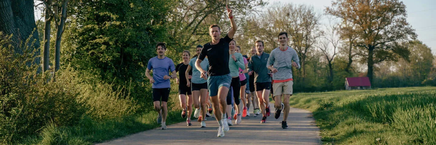 Eine Gruppe lächelnder Läufer und Läuferinnen joggt über einen Feldweg.