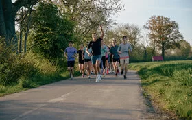 Eine Gruppe lächelnder Läufer und Läuferinnen joggt über einen Feldweg.