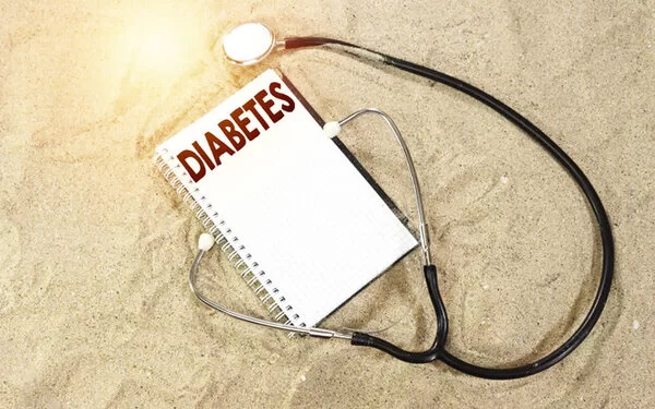 Diabetes-Tagebuch und Stethoskop liegen im Sand