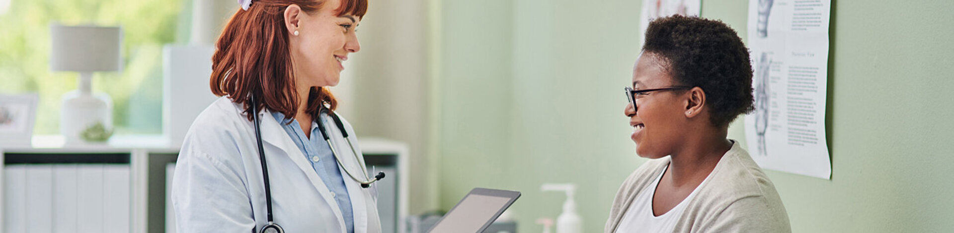 Eine Ärztin spricht mit einer Patientin, die auf einer Liege im Behandlungsraum sitzt.