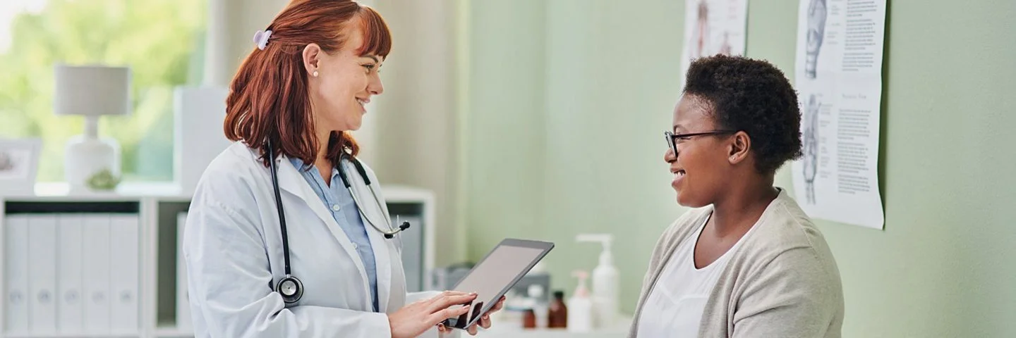 Eine Ärztin spricht mit einer Patientin, die auf einer Liege im Behandlungsraum sitzt.