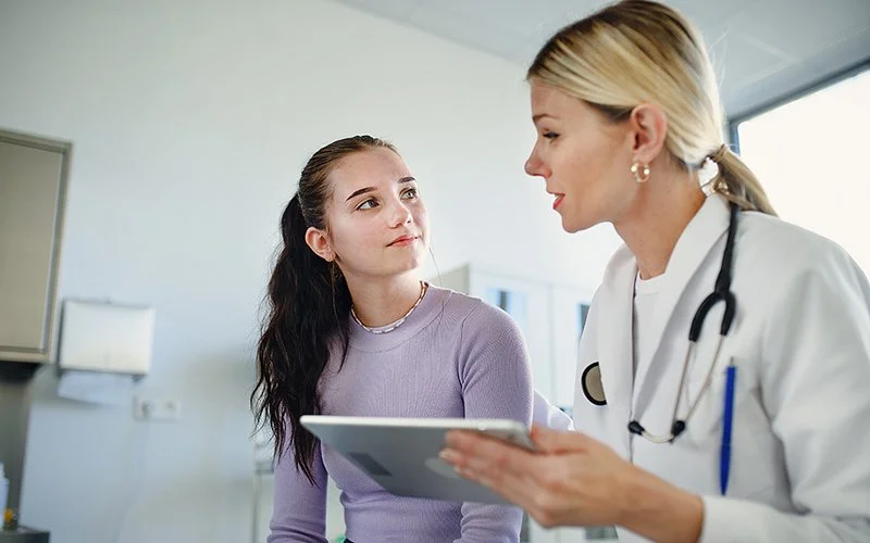 Eine Ärztin sitzt mit einem Tablet in der Hand neben einem Mädchen.