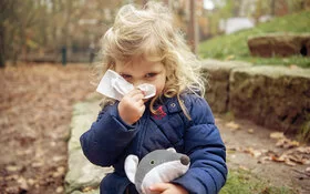 Ein Kind schnaubt sich die Nase mit einem Taschentuch.