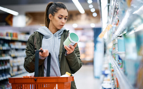 Junge Frau schaut im Supermarkt, ob Konservierungsstoffe in den Produkten enthalten sind.