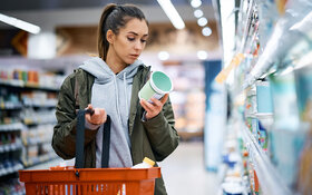 Junge Frau schaut im Supermarkt, ob Konservierungsstoffe in den Produkten enthalten sind.
