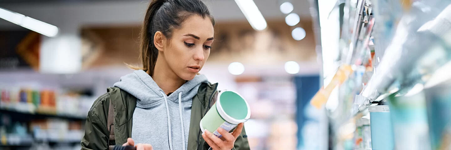 Junge Frau schaut im Supermarkt, ob Konservierungsstoffe in den Produkten enthalten sind.