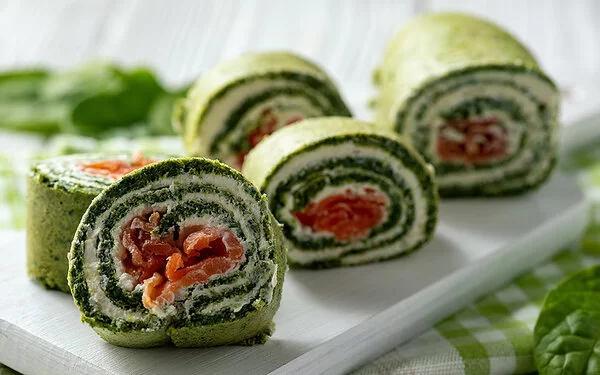 Spinat-Lachs-Rolle mit Kräuterfrischkäse auf weißem Brett.