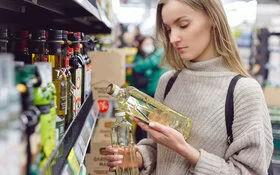 Eine junge Frau vergleicht im Supermarkt die Etiketten von zwei Ölflaschen.