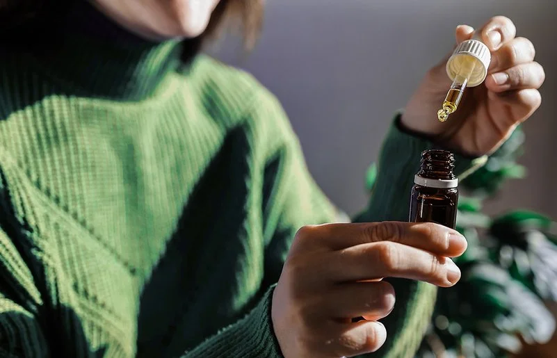 Eine Frau entnimmt aus einer kleinen braunen Flasche einige Tropfen Flüssigkeit mit einer Pipette.