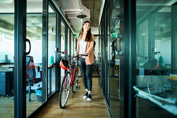 Eine Frau schiebt ihr Fahrrad als nachhaltiges Verkehrsmittel ins Büro.