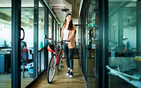 Eine Frau schiebt ihr Fahrrad als nachhaltiges Verkehrsmittel ins Büro.