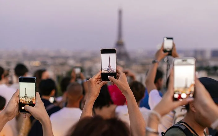 Mehrere Menschen halten ihr Smartphone in die Höhe, um den Eiffelturm zu fotografieren.