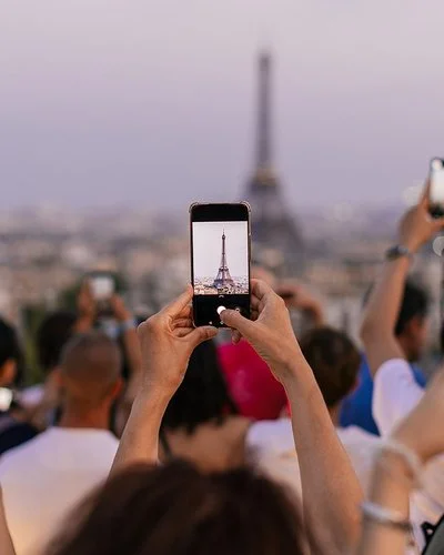 Mehrere Menschen halten ihr Smartphone in die Höhe, um den Eiffelturm zu fotografieren.