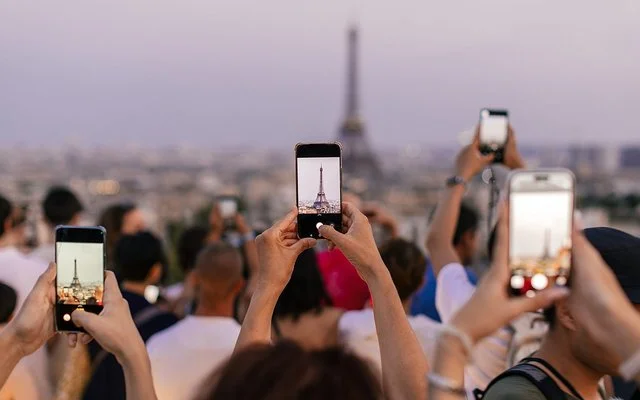 Mehrere Menschen halten ihr Smartphone in die Höhe, um den Eiffelturm zu fotografieren.