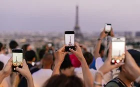 Mehrere Menschen halten ihr Smartphone in die Höhe, um den Eiffelturm zu fotografieren.