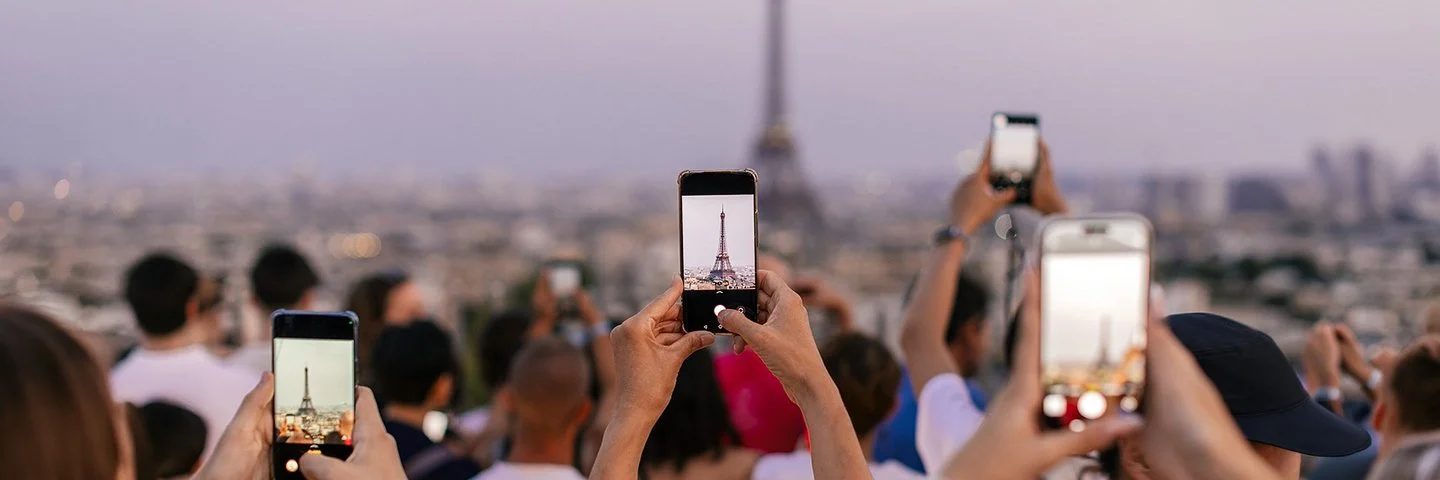 Mehrere Menschen halten ihr Smartphone in die Höhe, um den Eiffelturm zu fotografieren.