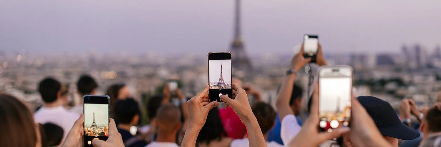 Mehrere Menschen halten ihr Smartphone in die Höhe, um den Eiffelturm zu fotografieren.