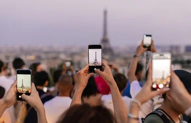 Mehrere Menschen halten ihr Smartphone in die Höhe, um den Eiffelturm zu fotografieren.