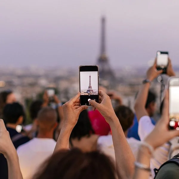 Mehrere Menschen halten ihr Smartphone in die Höhe, um den Eiffelturm zu fotografieren.