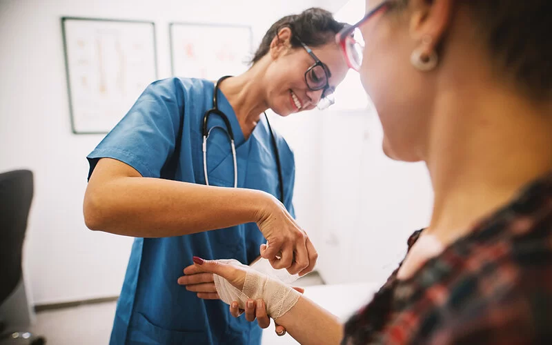 Eine Krankenschwester verbindet mit einer Mullbinde die rechte Hand einer Patientin.