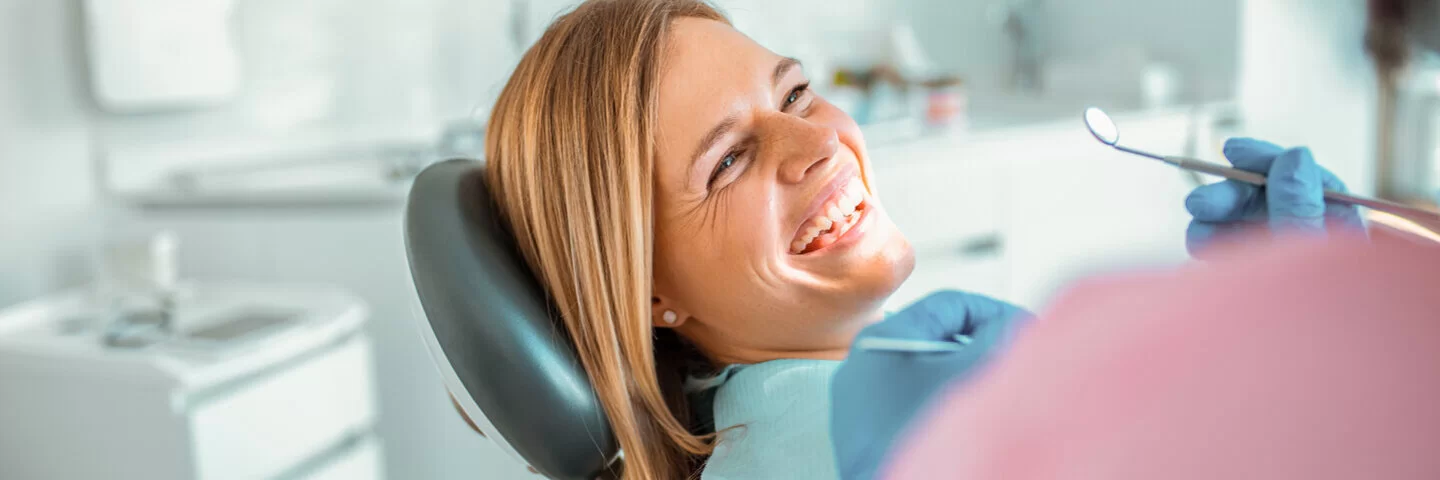 Eine Frau beim Zahnarztbesuch liegt auf einem Behandlungsstuhl und lächelt. Die AOK bietet über Kooperationspartner spezielle Zahnzusatzversicherungen an.