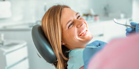 Eine Frau beim Zahnarztbesuch liegt auf einem Behandlungsstuhl und lächelt. Die AOK bietet über Kooperationspartner spezielle Zahnzusatzversicherungen an.