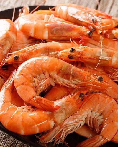 Nahaufnahme eines schwarzen Tellers mit ungeschälten Garnelen auf grobem Holzuntergrund.