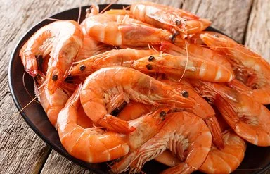 Nahaufnahme eines schwarzen Tellers mit ungeschälten Garnelen auf grobem Holzuntergrund.