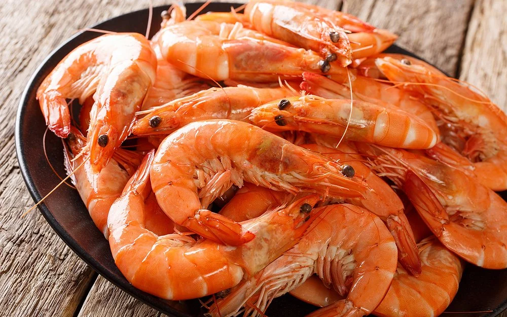 Nahaufnahme eines schwarzen Tellers mit ungeschälten Garnelen auf grobem Holzuntergrund.